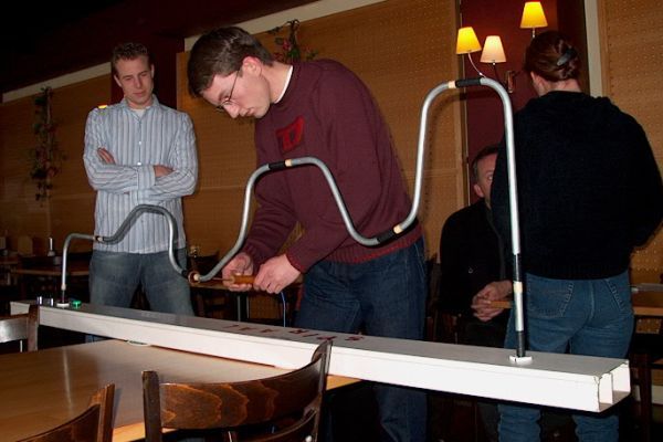 Mensen spelen een tafelspel waarbij ze een lus over een draadrail leiden.