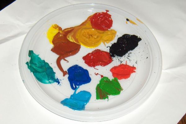 Palet met klodders verf in verschillende kleuren: geel, bruin, rood, zwart, groen, blauw en turquoise.