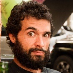 Um homem com barba e cabelo cacheado está fazendo uma careta engraçada.