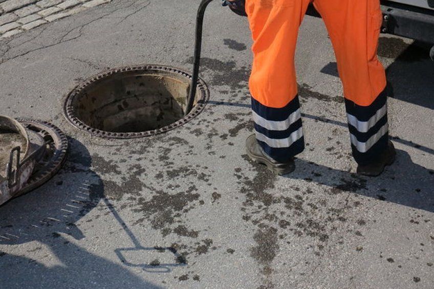 A man is standing next to a manhole cover on the side of the road.