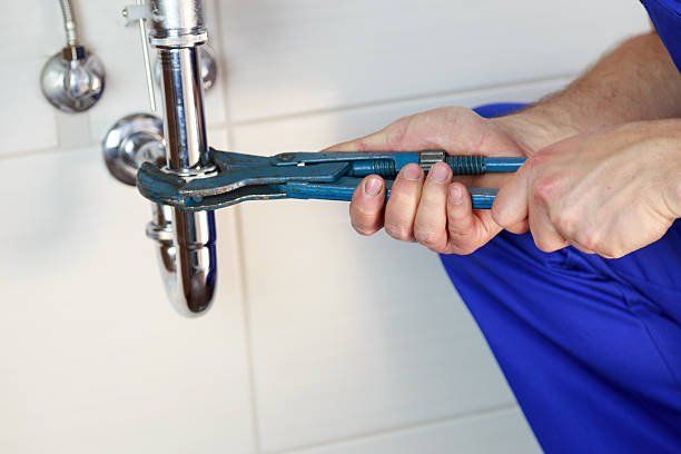 Plumber using wrench on chrome pipe.