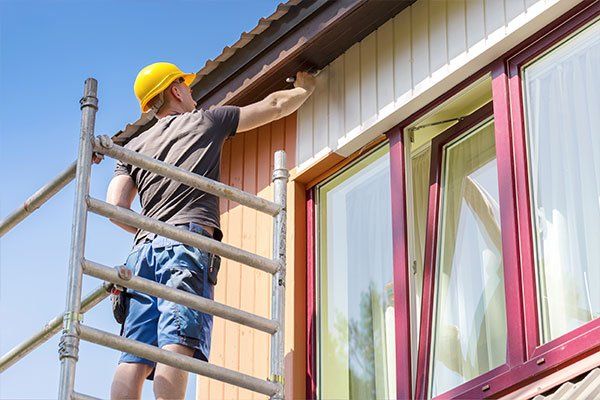 Worker on scaffolding painting wooden house