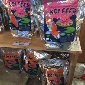 Bags of colorful koi feed displayed on a wooden shelf in a store.