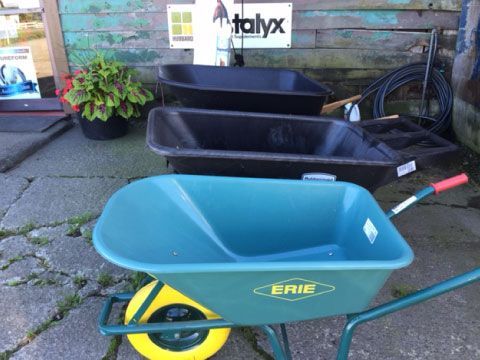 Blue Erie wheelbarrow in front of black wheelbarrows outside a store.