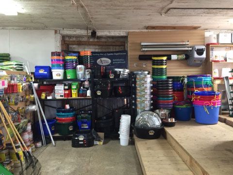 Store aisle with stacked bins, buckets, and cleaning supplies on shelves and the floor