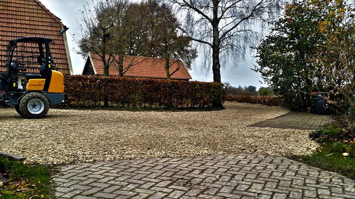 Een grindpad met aan de linkerkant een geel bouwvoertuig geparkeerd.