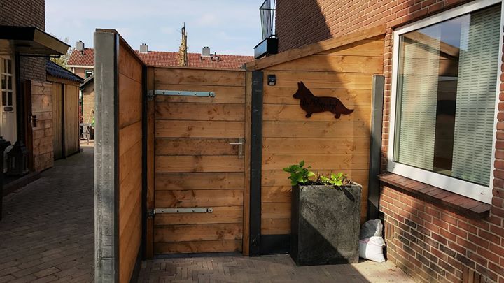 Houten hek met een hondensilhouet, naast een gebouw en een steegje.