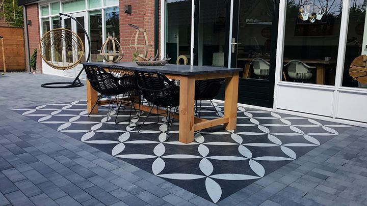 Terras met zwart-witte tegels in patroon, een houten tafel, zwarte stoelen en een hangstoel.