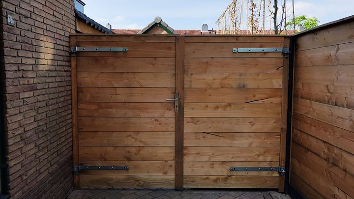 Een houten dubbele poort in een smalle doorgang, geflankeerd door bakstenen en houten muren.