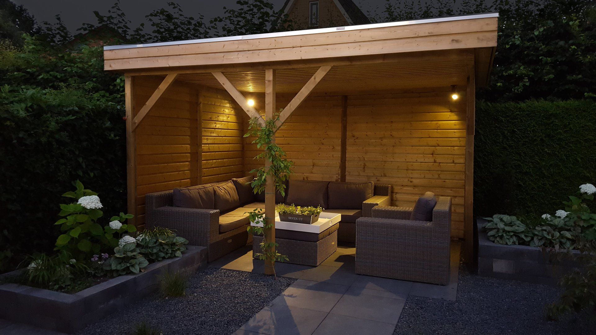 Houten tuinpaviljoen met zitgelegenheid en sfeerverlichting.