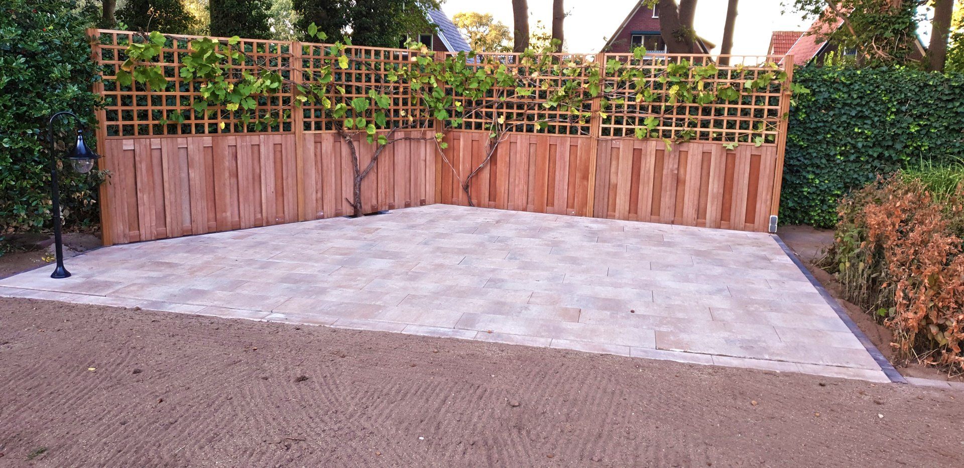 Houten schutting met latwerk bovenaan, stenen terras en groen.