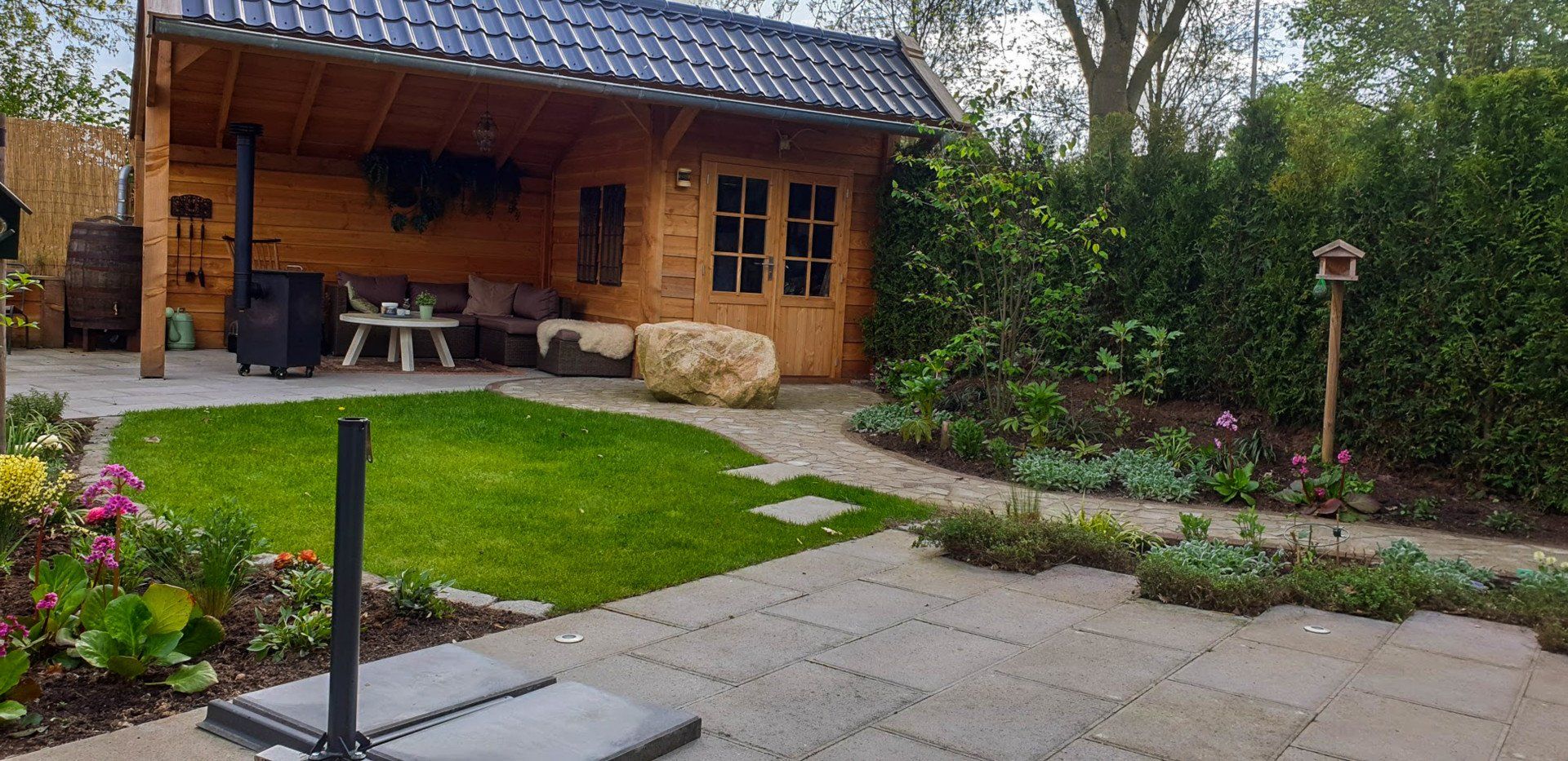 Gezellige achtertuin met een houten blokhut, groen gazon, betegeld terras en tuinpad.