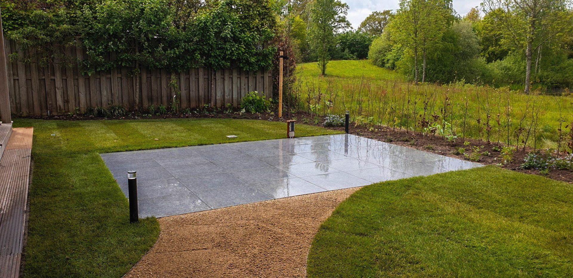 Een achtertuin met een stenen terras, gras, een grindpad en een houten schutting.
