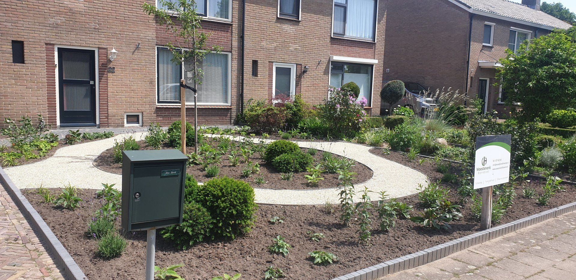 Een huis in een buitenwijk met een donkergroene brievenbus voor een kronkelend bakstenen pad door een tuin.
