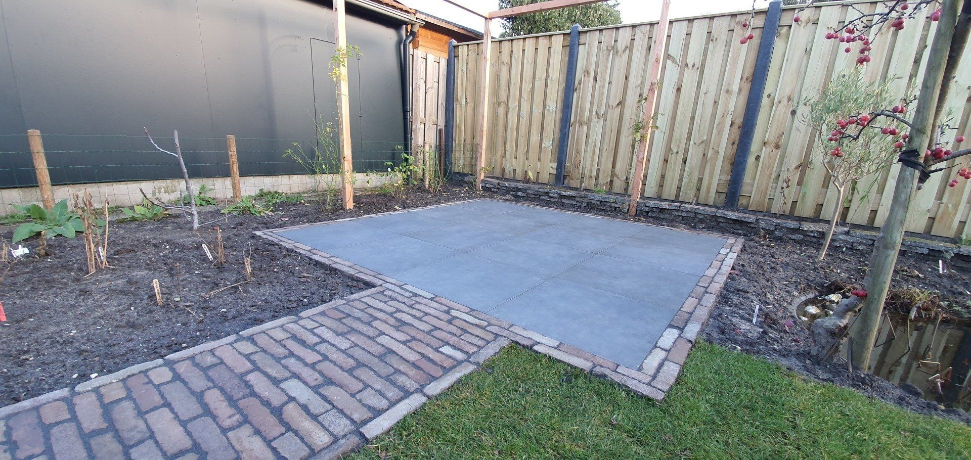 Een terras in de achtertuin met een bakstenen pad en een houten schutting.