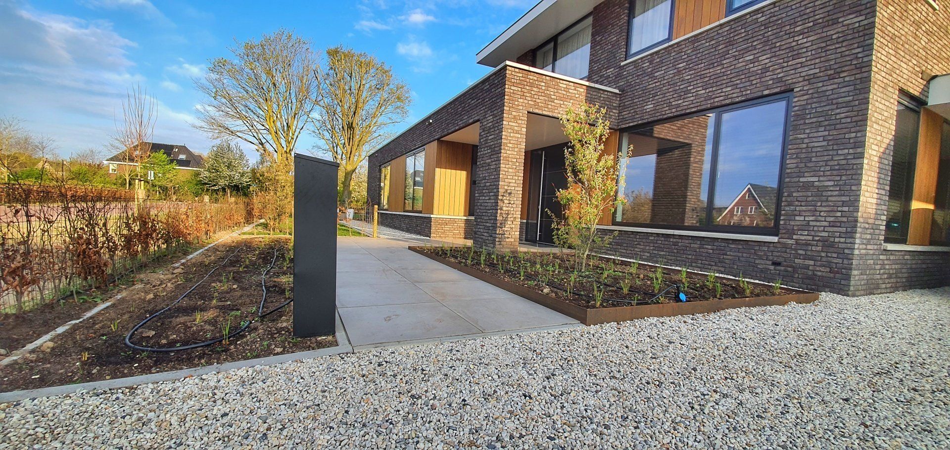 Moderne bakstenen woning met een oprit van grind en een beplante border onder een blauwe hemel.