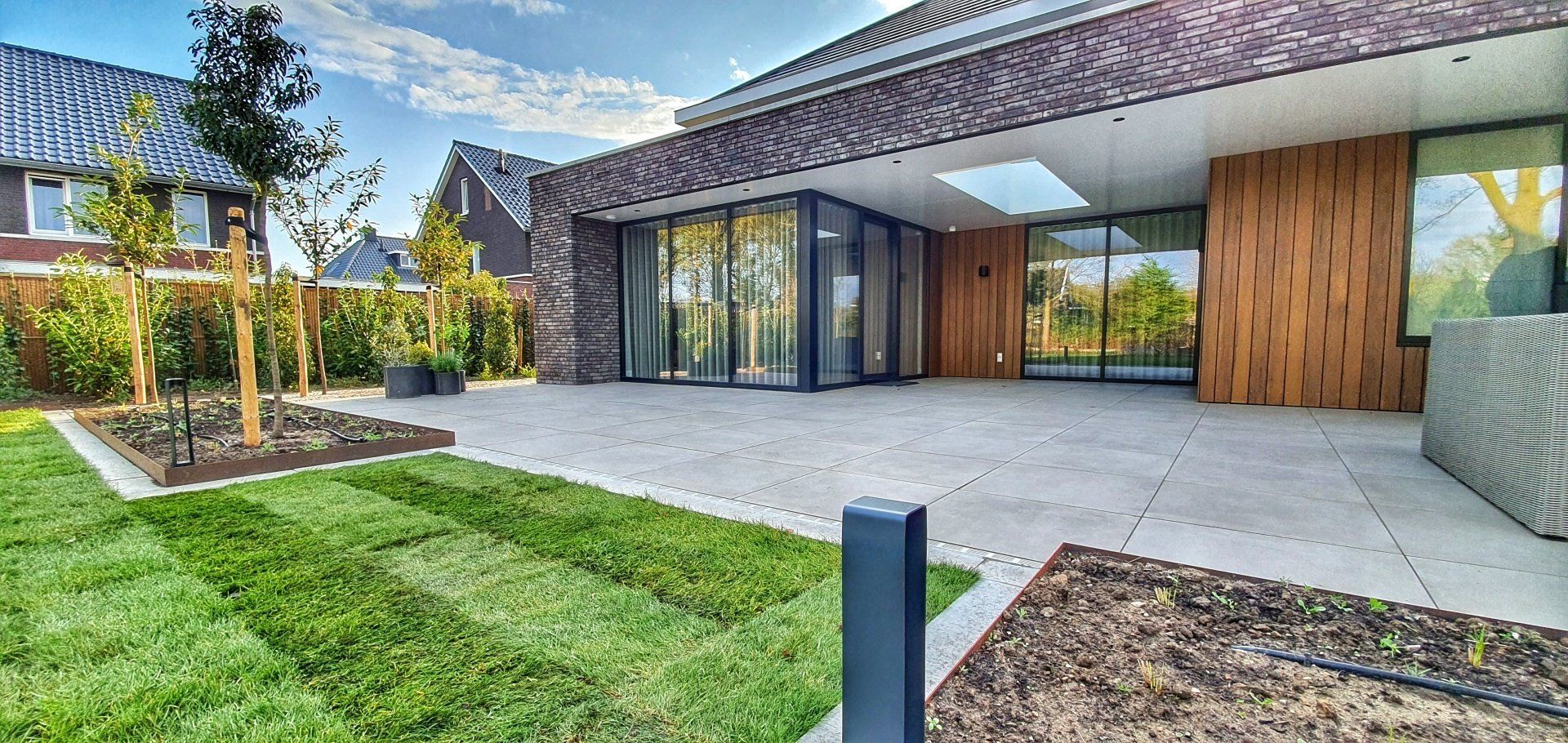 Moderne woning met een groot terras en een groen gazon. Houten gevelbekleding en grote ramen zijn zichtbaar.