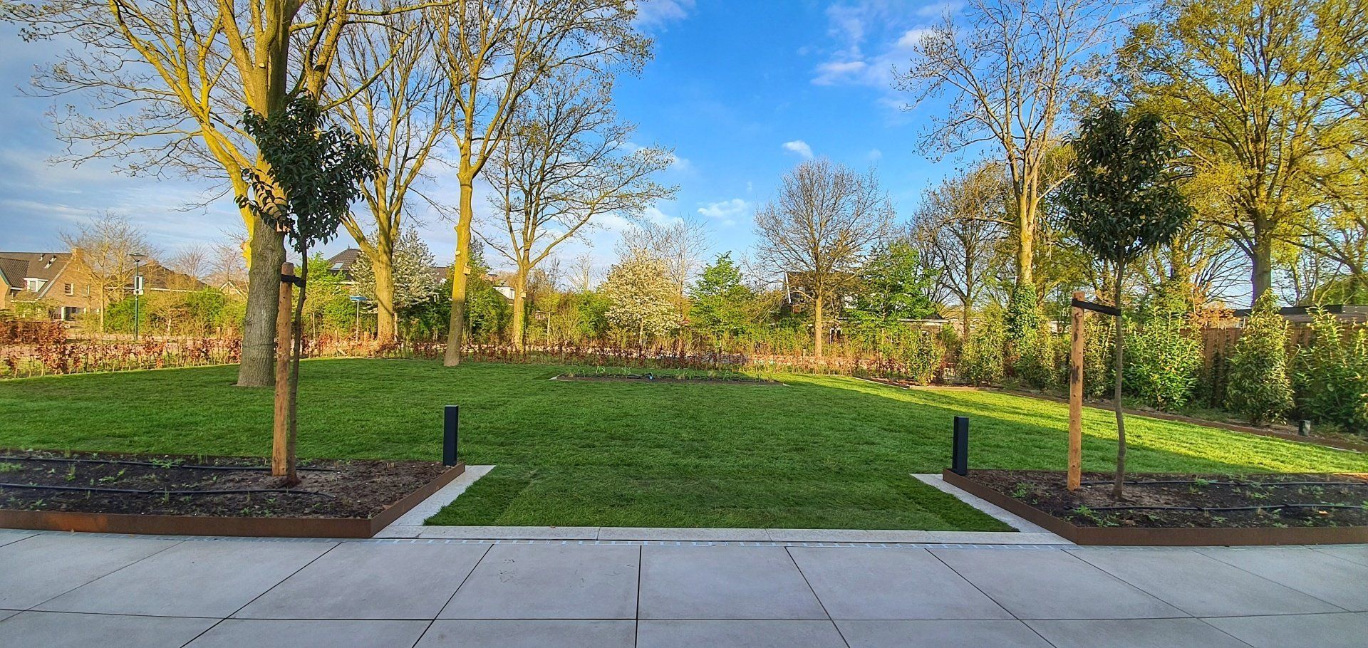 Een groen gazon tussen beton en bomen onder een blauwe hemel.