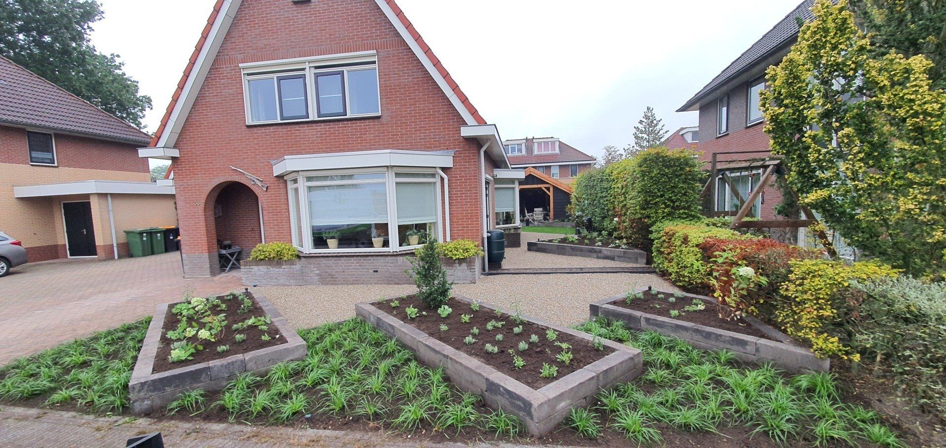 Een bakstenen huis met een driehoekig dak en een oprit met drie verhoogde bloembedden.