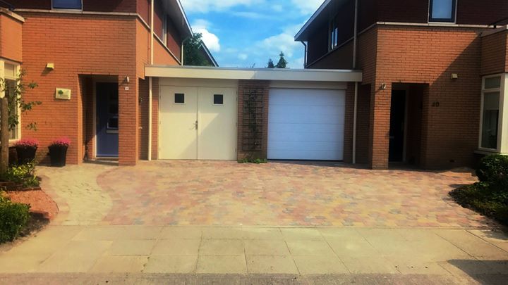 Bakstenen rijtjeshuizen met gedeelde garage en oprit van bakstenen onder een blauwe hemel.