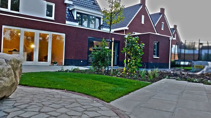 De buitenkant van een modern bakstenen huis met een groen gazon, een betegeld terras en diverse ramen.