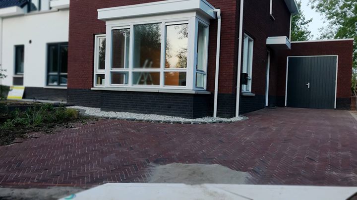 Moderne bakstenen woning met een donkere garagedeur, grote ramen en een bakstenen oprit.