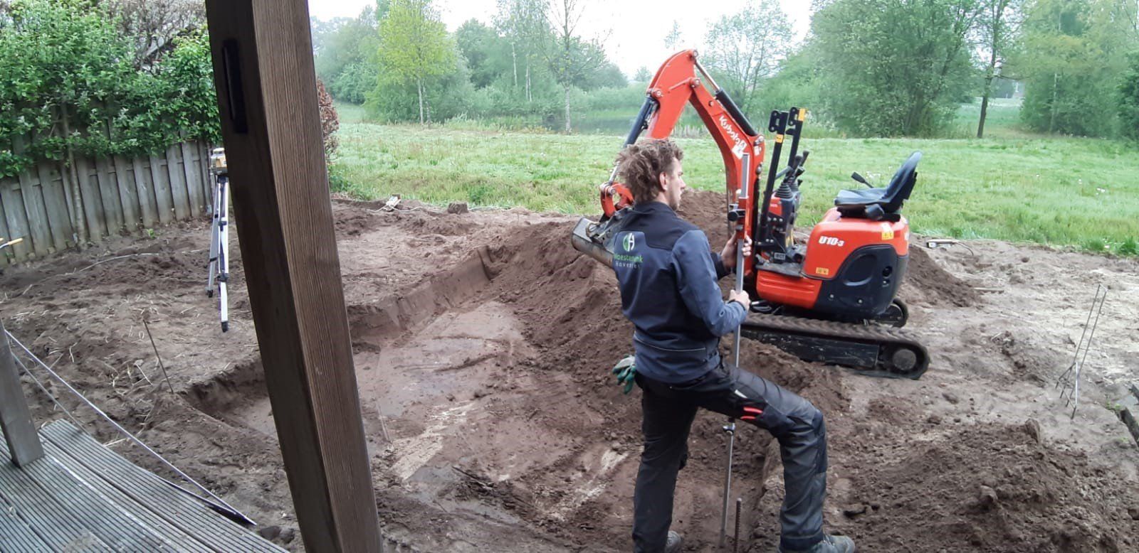 Een persoon bestuurt een oranje graafmachine op een modderig bouwterrein.