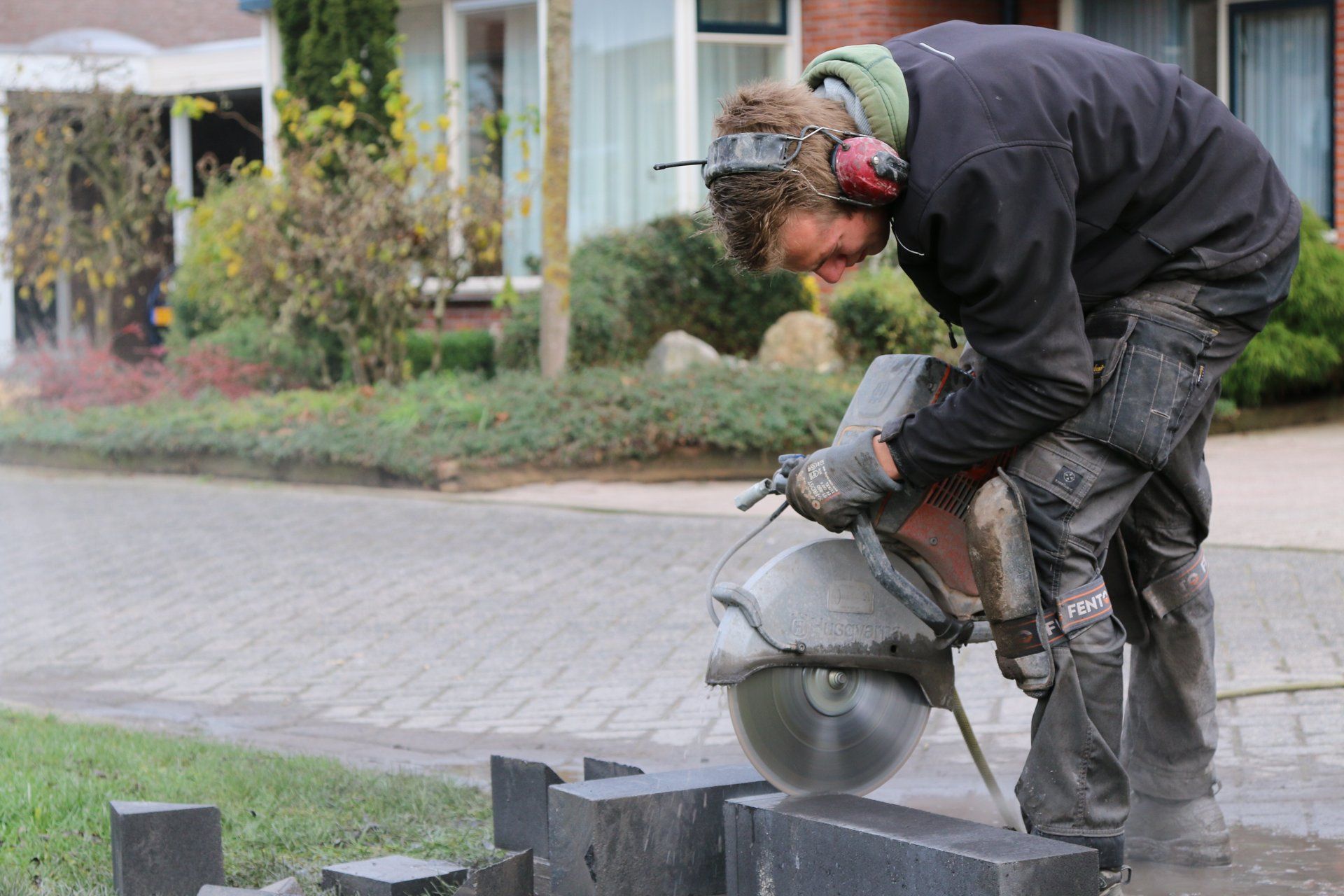 Een man zaagt buiten stenen blokken door met een motorzaag. Hij draagt ​​gehoorbescherming, handschoenen en werkkleding.