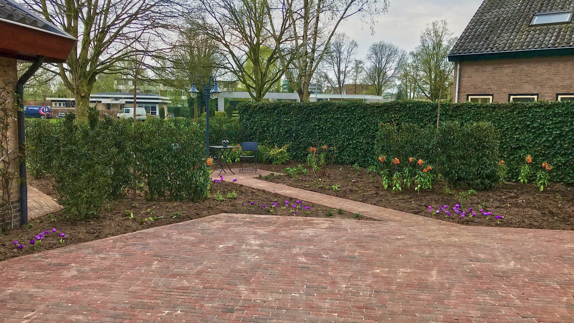 Een stenen terras leidt naar een tuin met groene hagen, tulpen en bomen.
