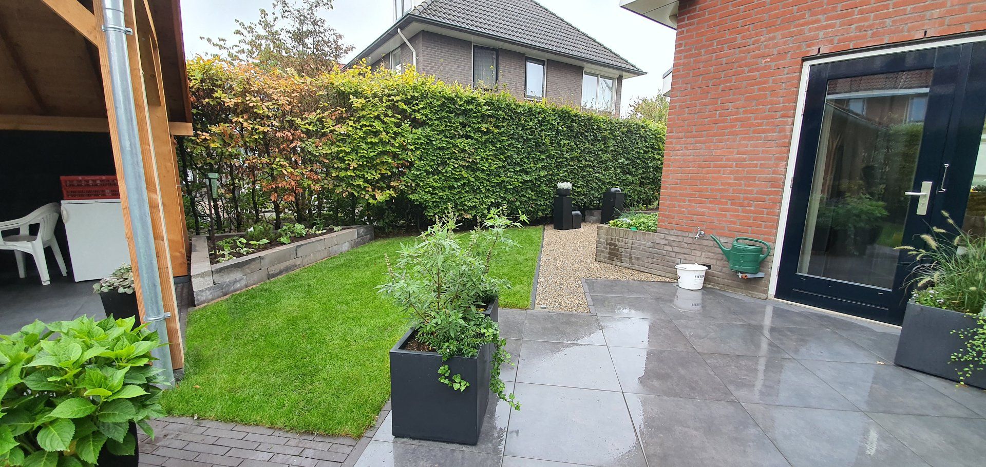 Een weelderige groene tuin met een stenen pad, een gazon en een rood bakstenen huis met een zwarte deur.
