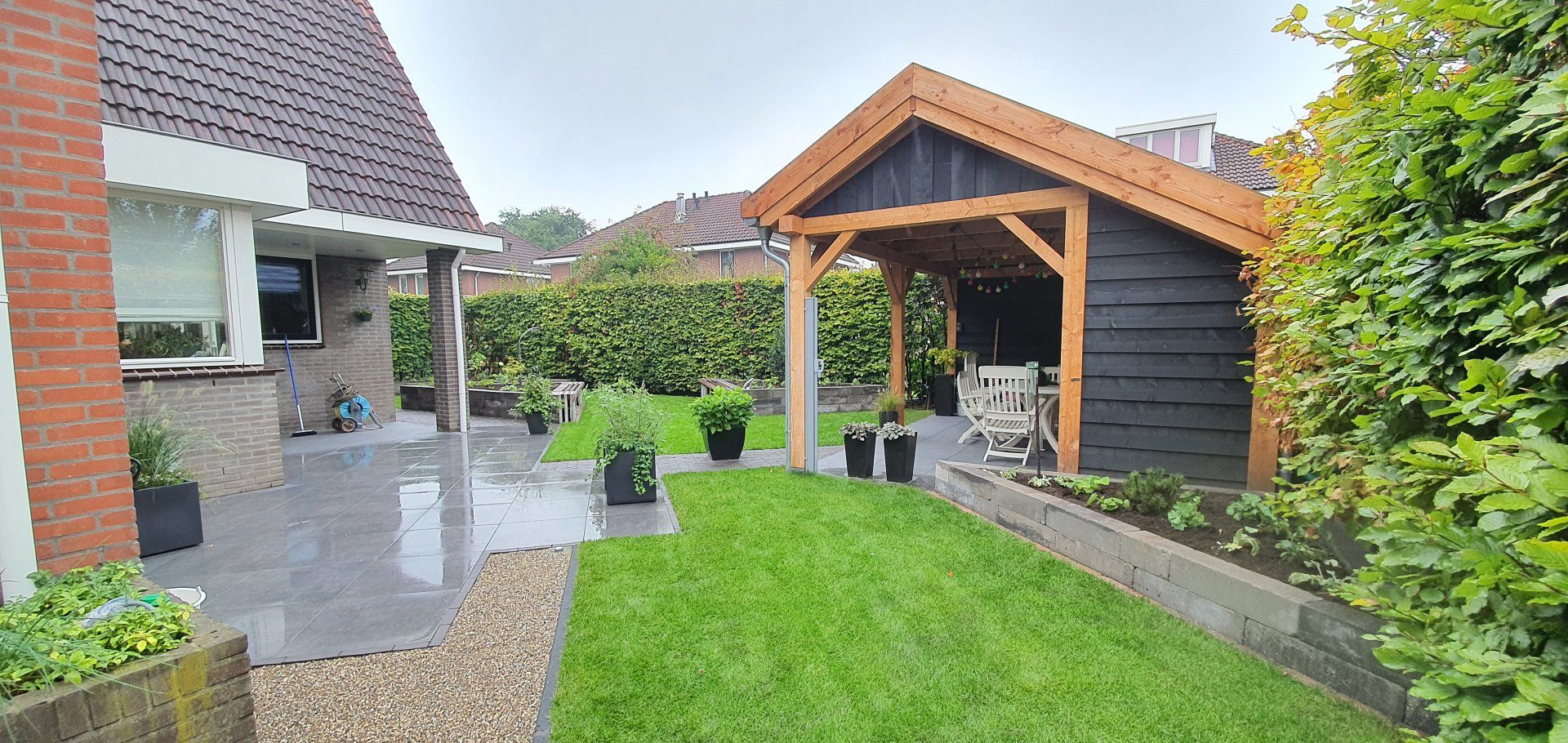 Een achtertuin met een terras, gazon en houten schuur op een bewolkte dag.