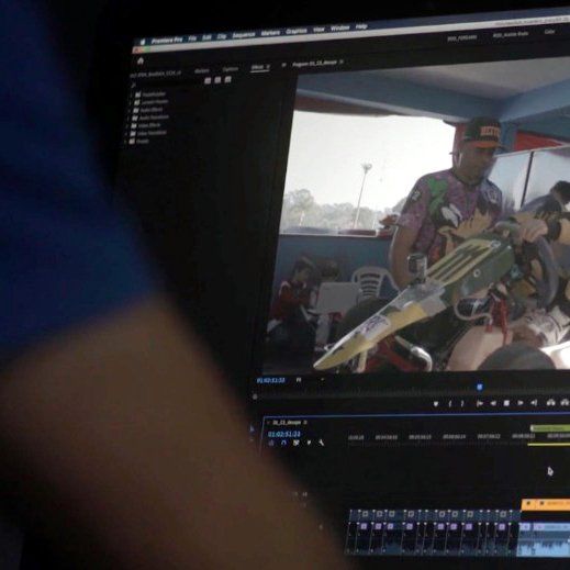 A computer screen shows a man holding a surfboard