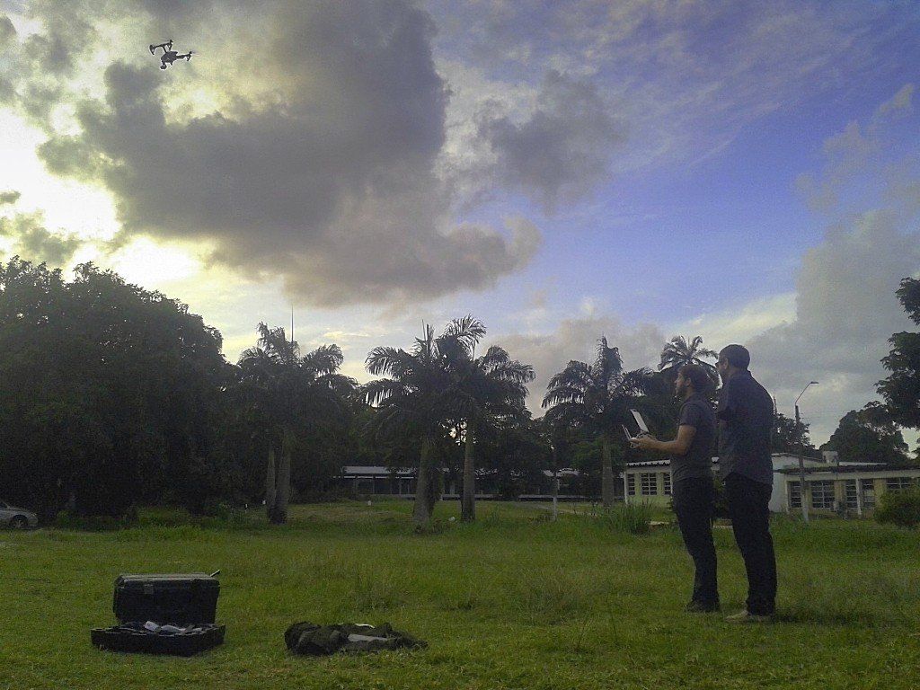 A man is standing in a grassy field watching a drone fly in the sky
