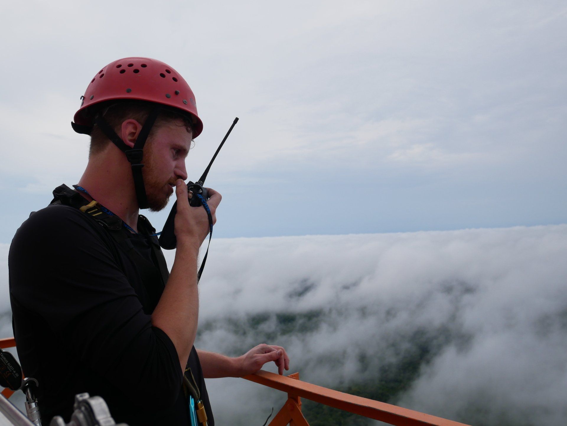A man wearing a red helmet is talking on a walkie talkie.
