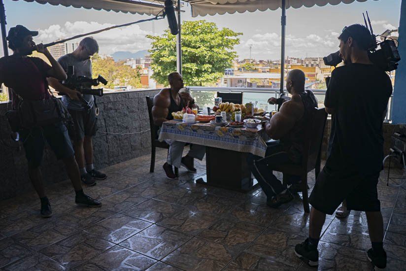 A group of people are sitting around a table while a cameraman takes a picture.