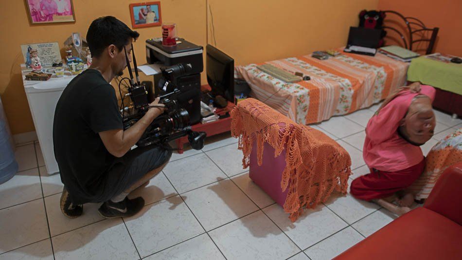 A man is kneeling down in front of a camera in a bedroom.