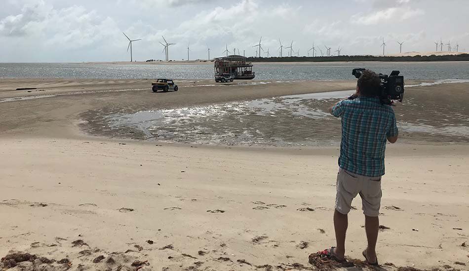 A man is standing on a beach holding a camera.