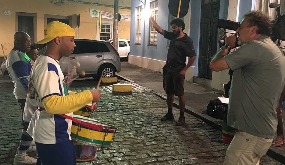 A group of people are standing on a cobblestone street playing drums.