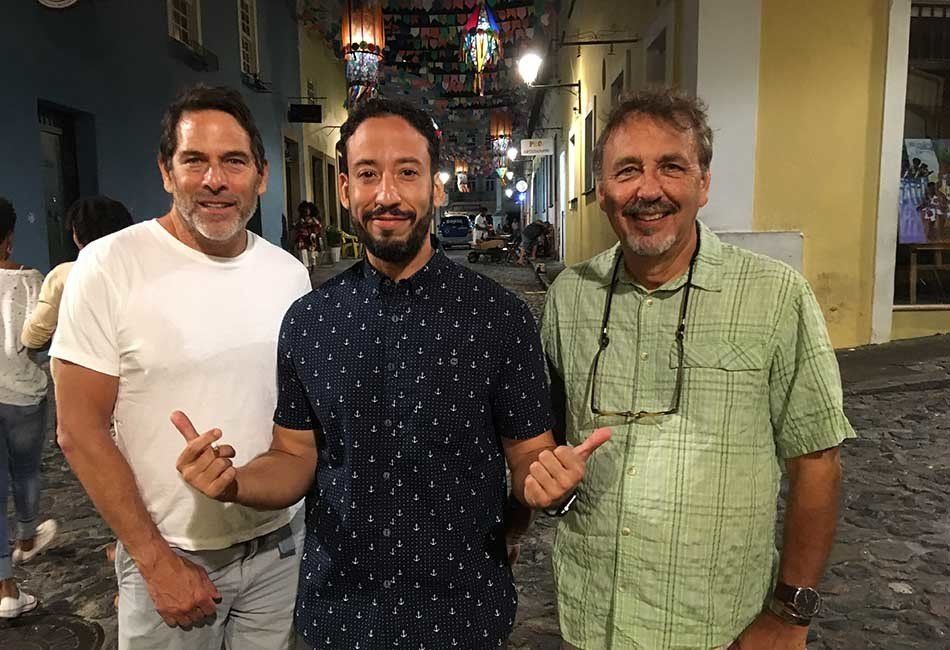 Three men are standing next to each other on a cobblestone street.