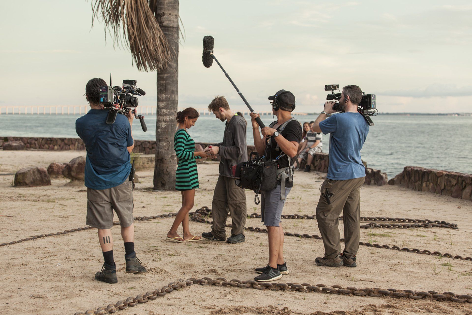 A group of people are standing on a beach with cameras and microphones.