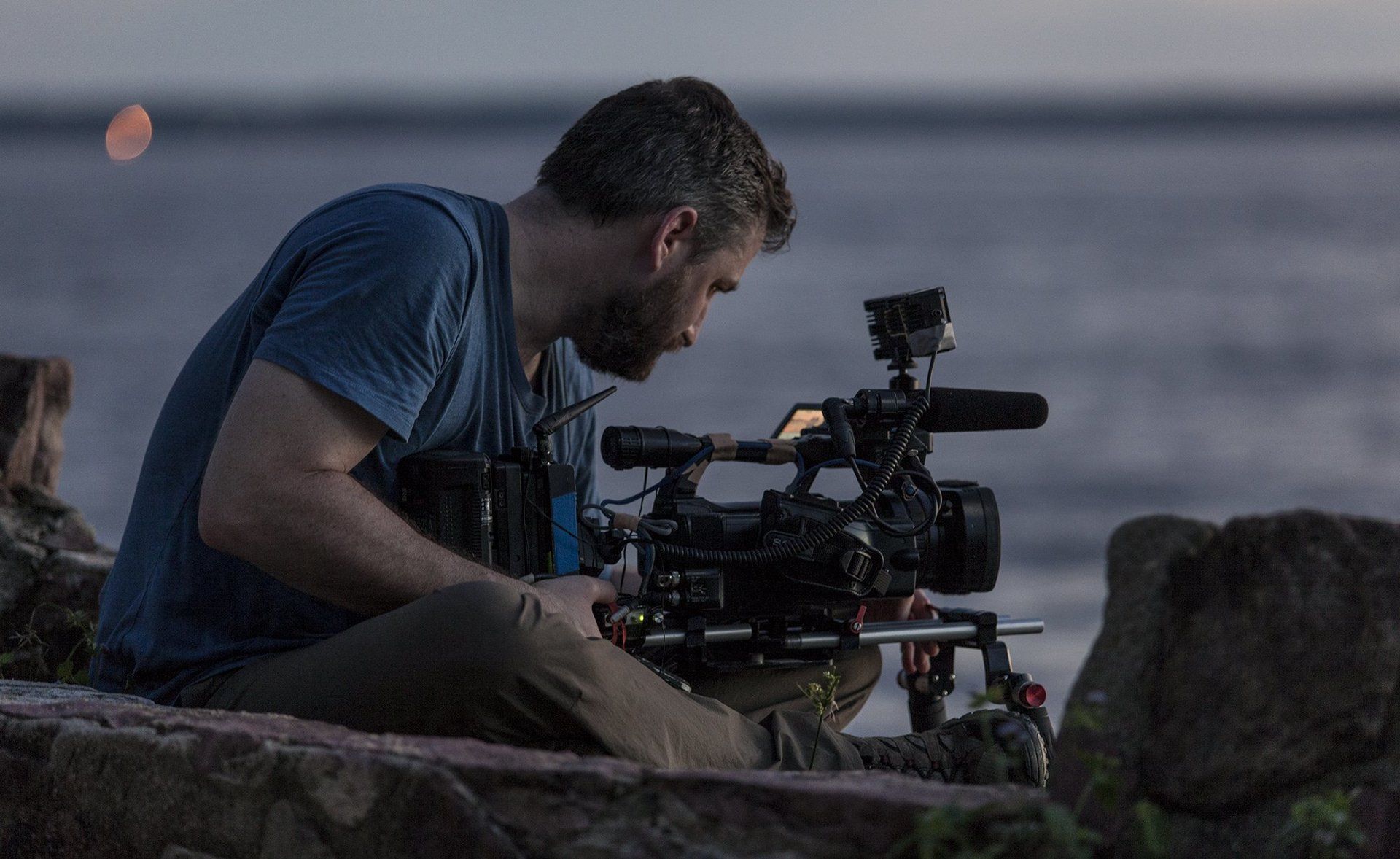 A man is sitting on a rock looking at a camera.