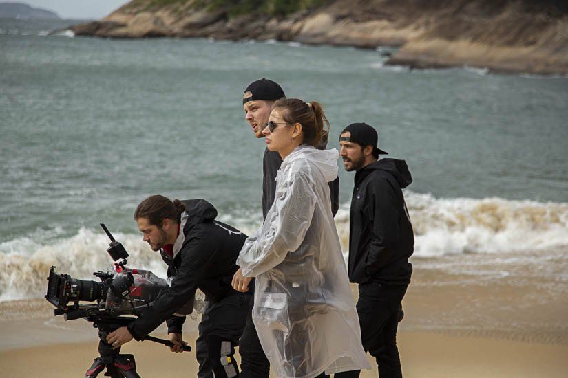 A group of people are standing on a beach looking at a camera.