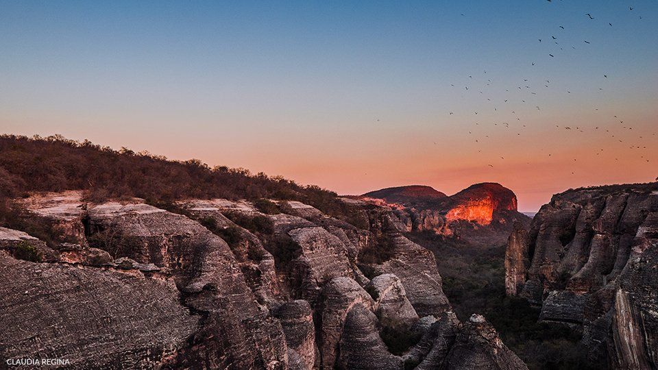 A sunset over a cliff with a mountain in the background.
