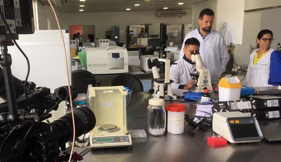A group of people are standing around a table in a lab looking through microscopes.