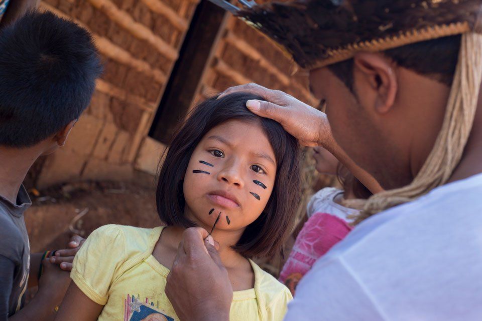 A man is painting a little girl 's face with black paint.