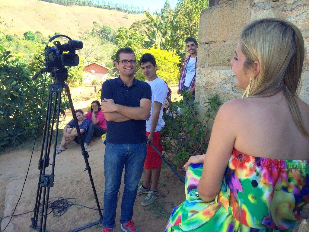 A woman in a colorful dress is talking to a man in front of a camera.