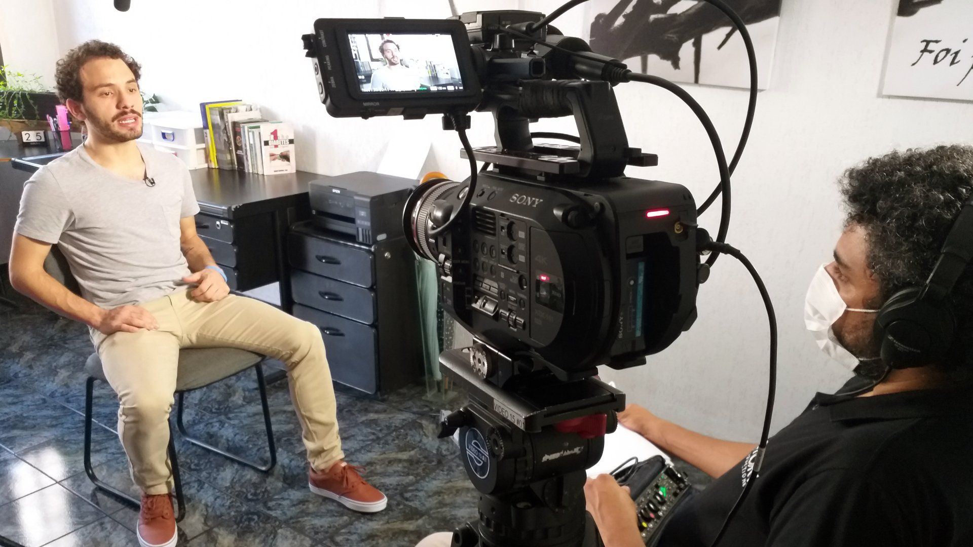 A man wearing a mask is sitting in front of a camera.