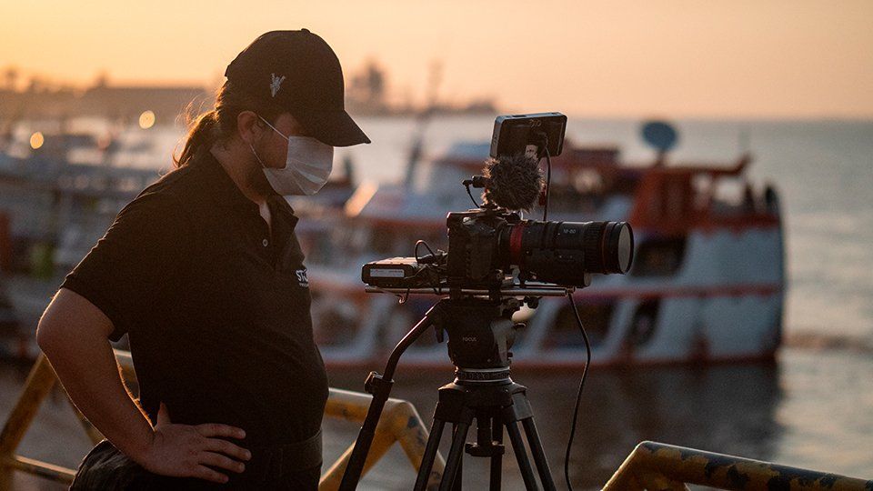 Story Productions crew films on location in Santarém A man wearing a mask is standing in front of a camera on a tripod.