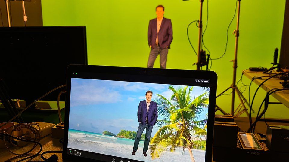 Story Productions crew films on set A man in a suit is standing on a beach in front of a green screen.