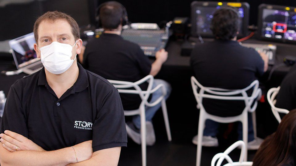 Story Productions crew works on location in a live streming project A man wearing a mask is standing in front of a group of people.